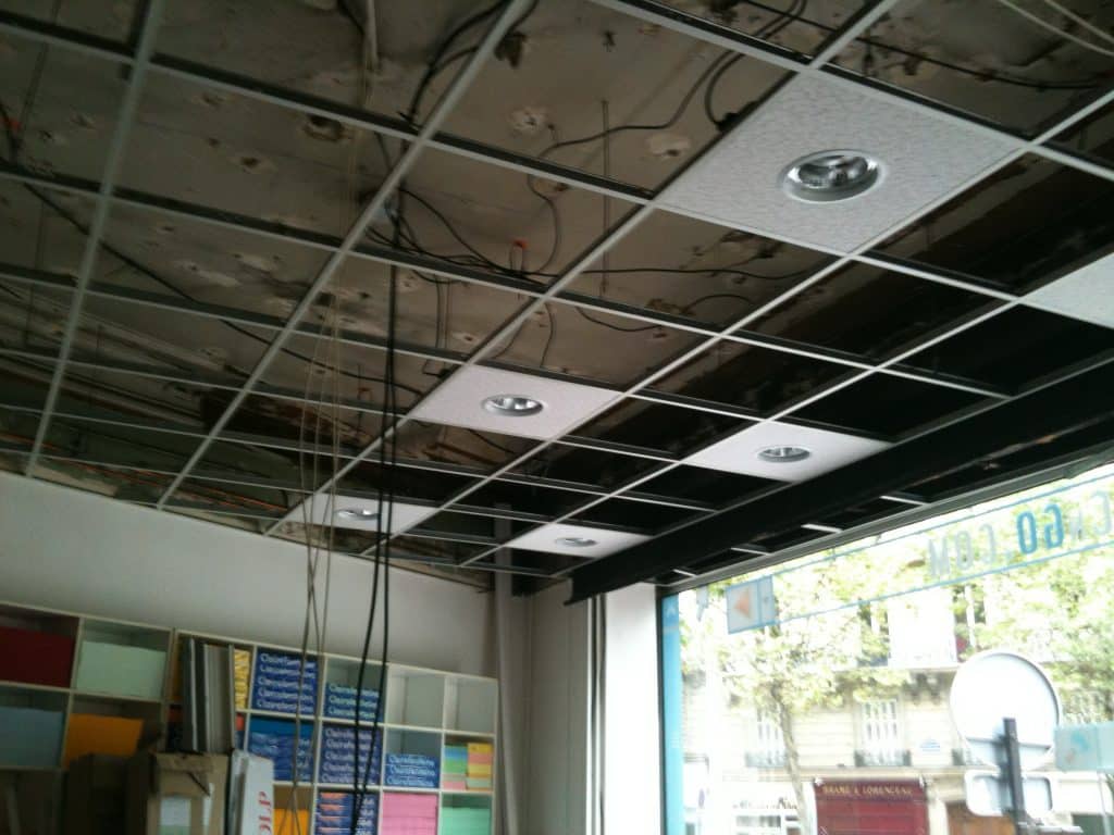 Installation électrique de luminaires encastrés dans un faux plafond démontable, câblage visible au-dessus des dalles